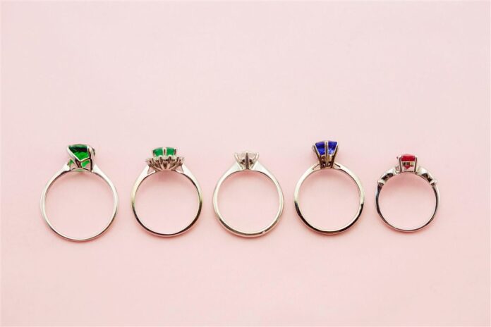 AdobeStock_120662976 Five gemstone rings arranged side by side on a pink background