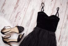 Black dress and matching heeled sandals arranged on pale wooden boards
