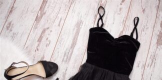 Black dress and matching heeled sandals arranged on pale wooden boards
