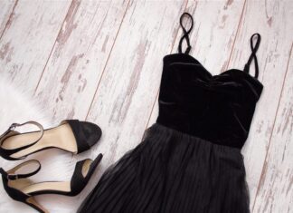 Black dress and matching heeled sandals arranged on pale wooden boards