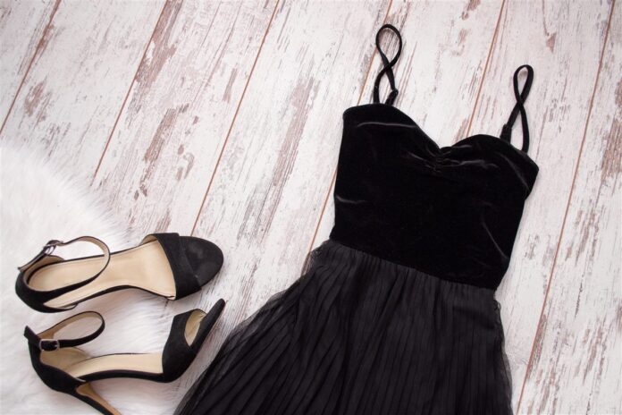 AdobeStock_137236381 Black dress and matching heeled sandals arranged on pale wooden boards
