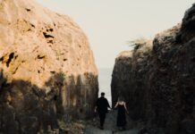 Planning an Active Honeymoon When You Enjoy Different Sports Couple holding hands on a rocky coastal path towards the sea