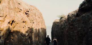 Planning an Active Honeymoon When You Enjoy Different Sports Couple holding hands on a rocky coastal path towards the sea
