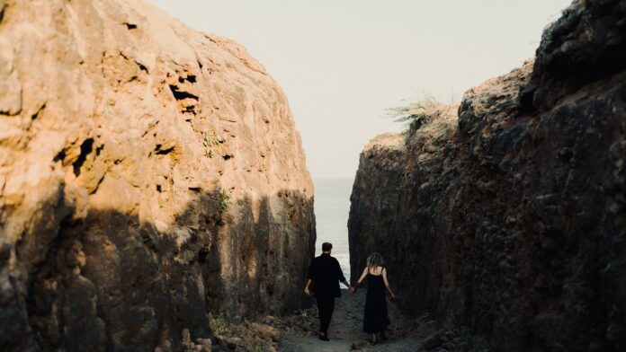 Couple holding hands on a rocky coastal path towards the sea